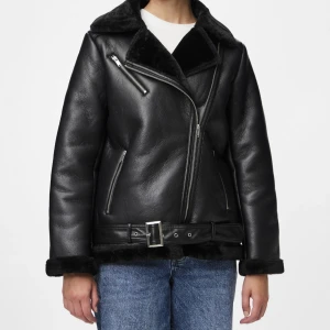 Svart pälsjacka med bälte och dragkedjor - Säljer en svart pälsjacka med bred krage och mjuk päls på insidan. Jackan har flera silvriga dragkedjor, bälte i midjan och detaljer vid ärmslut och nederkant. Snygg oversized passform som ger en cool vibe och passar perfekt till jeans.