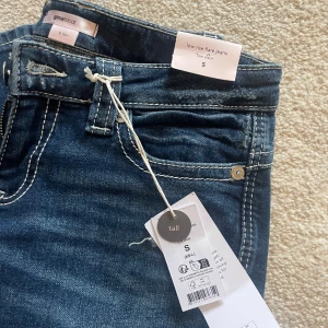 Low rise flare jeans från Gina Tricot - Säljer ett par blå low rise flare jeans från Gina Tricot i storlek S tall. Jeansen har slitna detaljer och hål på knäna, kontrastsömmar och klassisk femficksdesign. Modellen har låg midja och utsvängda ben för en riktigt snygg 00-talsvibe. LÅNGA PÅ MIG SOM ÄR 173. 