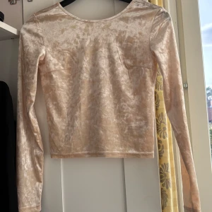 Beige sammetstopp med lång ärm - Säljer en ljusbeige croppad topp i mjuk sammet med lång ärm och rundad urringning på baksidan . Toppen har en lätt glansig yta och figurnära passform. Aldrig använt