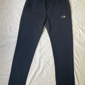 Marinblå mjukisbyxor från The North Face - Marinblå mjukisbyxor från The North Face med dragsko i midjan och två sidofickor. Byxorna har reflex-aktig logga på vänster lår och är tillverkade i galet mjukt och bekvämt material. Passar storlek L-XL