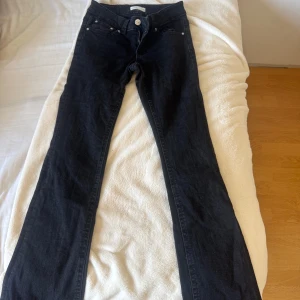 Svarta bootcut jeans från Gina Tricot - Snygga svarta jeans från Gina Tricot, modell Perfect Jeans. Bootcut passform med klassiska fem fickor och coola bakfickor med lock och knapp. Jeansen har dragkedja och knapp framtill och är gjorda i mjukt denimtyg. Är använd 2 gånger 