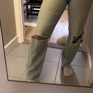 Ljusblå high waist jeans med hål - Säljer ett par ljusblå jeans med hög midja och raka ben. Jeansen har slitna hål över knäna för en trendig look och är tillverkade i klassisk denim. 