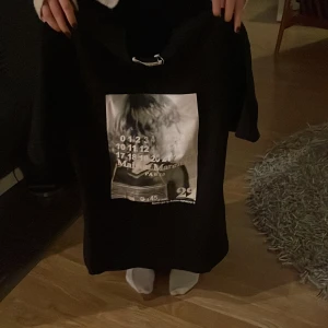 Masion margiella T-shirt - Svart t-shirt med stort grafiskt print framtill och vita sömmar i nacken på baksidan. Tröjan har snörning vid halsen och en loose passform, perfekt för dig som gillar streetwear och coola designer.