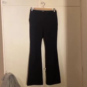 Svarta bootcut kostymbyxor från ONLY - Svarta kostymbyxor från ONLY med bootcut-ben och klassisk passform. Byxorna har dragkedja och knapp framtill samt hällor för bälte. Snyggt skräddad modell som ger en clean och stilren look. Dragkedjan är ny syd proffesionellt.