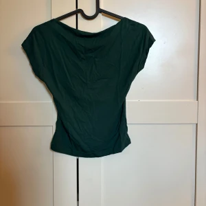 Mörkgrön topp med öppen rygg - Snygg mörkgrön topp med korta ärmar och en djup öppen rygg. Enkel men ändå unik detalj med den öppna ryggen som ger en cool twist.