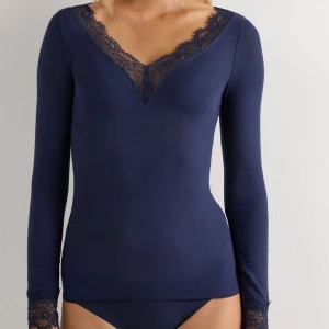 Marinblå långärmad topp med spets från intimissimi  - Snygg marinblå långärmad topp med djup v-ringning och spetsdetaljer både vid halsringningen och ärmsluten. Toppens material är mjukt och stretchigt, vilket gör den bekväm att bära. Perfekt för dig som gillar en feminin och stilren look. Några hål vid armen, se bild 3 som jag försökt sy igen. Därav priset. Annars bra skick. 