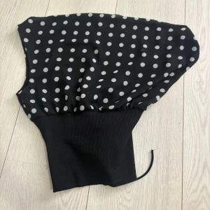 Design by Si - Snygg svart korsettopp med vita prickar och bred ribbad midja. Toppen har snörning i ryggen för en justerbar passform och är ärmlös med en croppad siluett. Perfekt för att skapa en cool och trendig look. Aldrig använd!