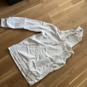 Vit hoodie från Peak Performance - Säljer en stilren vit hoodie från Peak Performance i mjuk bomull. Tröjan har huva med snörning, magficka och klassisk passform. Perfekt för dig som gillar en clean och enkel look. Storlek M.