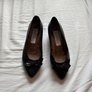 Svarta ballerinaskor från Frans! - Klassiska svarta ballerinaskor i skinn från Frans! Copenhagen. Skorna har spetsig tå och en söt rosett framtill som ger en elegant touch. Perfekta för dig som gillar stilrena och tidlösa detaljer. Insidan är metallicfärgad för en extra lyxig känsla 😌