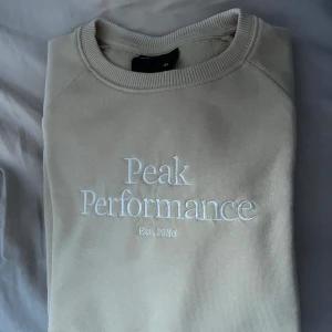 Beige Peak Performance sweatshirt - Säljer en beige sweatshirt från Peak Performance med broderad logga och text på bröstet. Tröjan har rund halsringning, långa ärmar och är gjord i mjuk bomullsmix. Perfekt för chill dagar eller när du vill ha en clean och enkel stil.
