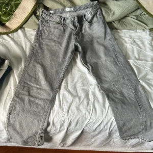 Grå jeans från Jack & Jones - Snygga grå jeans från Jack & Jones med klassisk femficksdesign och raka ben. Jeansen har normal passform och är tillverkade i mjukt denimtyg som ger en avslappnad vibe. Perfekta för dig som gillar stilrena och enkla jeans.