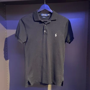 Svart pikétröja Polo Ralph Lauren XS - Klassisk svart pikétröja från Polo Ralph Lauren i slim fit. Tröjan har korta ärmar, krage med knappar och den ikoniska broderade loggan i vitt på bröstet. Tillverkad i mjuk bomull som är skön mot huden. 8/10 skick och har inte fått mycket användning. Har man några frågor eller funderingar är det bara att höra av sig 👍