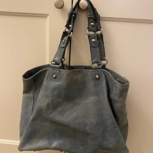 Blå skinnväska från Zadig & Voltaire - Cool blå axelväska i skinn från Zadig & Voltaire med robusta handtag och snygga metalldetaljer. Väskan har ett innerfoder i vinrött tyg med tryck och en praktisk innerficka med dragkedja. Perfekt för dig som vill ha en rymlig och stilren väska.