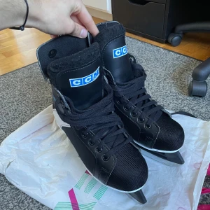 Svarta CCM Fury skridskor med skydd - Säljer ett par svarta och vita CCM Fury skridskor i storlek 40. Klassisk modell med snörning, robust ovandel i syntet och skinn, samt mjuk vadderad plös. Lite skadade båda skorna samma ställe (se bild) Medföljer vita och röda skydd till skenorna. Perfekta för vinterns isäventyr!