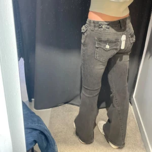 True Religion Joey Low Rise Flare Jeans - Snygga svarta jeans från True Religion, modell Joey Low Rise Flare. Byxorna har låg midja och utsvängda ben, klassiska silverfärgade knappar och detaljerade bakfickor med signatursöm. Perfekta för dig som gillar en cool och avslappnad stil. Uppsydda längst ner ca 5cm. Hör av er vid minsta fråga eller fundering. W29🌸