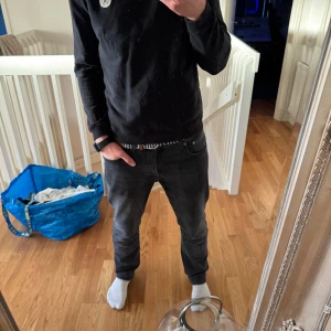 Svart parkajacka med dragkedja - Svart parkajacka med hög krage, fyra stora fickor framtill och axelklaffar. Jackan har både dragkedja och knappar framtill för extra stil och funktion. Tillverkad i bomullsmaterial och har en clean, urban look som passar perfekt till höst och vår. Om du har några frågor är det bara att höra av sig🫡