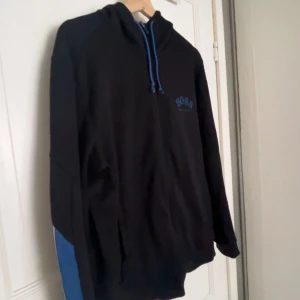 Limited edition kofta från Hugo Boss  - Limited edition Svart/blå kofta från Hugo Boss, blå snören och blå logga på bröstet. Tröjan har dragkedja framtill, huva med blå insida och blåa detaljer längs ärmarna. Perfekt för en chill och stilren look. Pris går att diskutera.