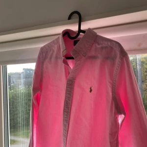 Rosa skjorta från Polo Ralph Lauren - Klassisk rosa skjorta från Polo Ralph Lauren. Skicket är 10/10 endast använd 1 gång! Strl är 14-16 vilket motsvarar s ungefär. Jag är 172 och den passar fint. Tveka inte på att höra av er för frågor. Fraktar 1-3 dagar.