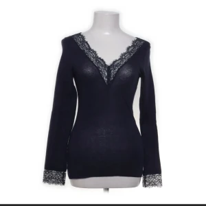 Mörkblå långärmad topp med spets - Snygg mörkblå långärmad topp med v-ringning och dekorativ spets både vid halsringningen och ärmsluten. Toppens smickrande passform och tunna material gör den perfekt för att styla med jeans eller kjol. Spetsdetaljerna ger en extra touch av elegans.