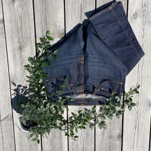 Mörkblå jeans från Nudie Jeans, W28 L32 - Säljer ett par mörkblå jeans från Nudie Jeans i modellen W28 L32. Jeansen är tillverkade av 100% ekologisk bomull och har klassiska orangea sömmar, fem fickor och Nudie-logga på bakfickan. Snygg, stilren look med raka ben och robust denimkänsla.