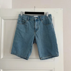 Blå jeansshorts från ASOS DESIGN - Klassiska blå jeansshorts från ASOS DESIGN med fem fickor och normal passform. Shortsen har gylf med dragkedja och knapp, samt bälteshällor. Perfekta för en avslappnad stil under varma dagar.