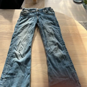 Blå jeans från Gina Tricot, stl 146 - Snygga blå jeans från Gina Tricot i storlek 146. Klassisk femficksmodell med dubbla knappar i midjan och raka ben. Jeansen har en cool tvätt och är tillverkade i mjukt denimtyg som är skönt att bära hela dagen. En liten fläck på ena låret. 