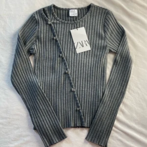 Grå ribbad topp med knappar från Zara - Supersnygg grå ribbad topp från Zara barn med knappar. Första bilden är lånad💕den är i Stolek 13-14 år, 164 cm men jag skulle säga att den passar Stolek S. 
