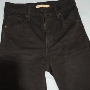 Levi's Mile High Super Skinny Jeans Hög Midja, Svart S 36 / (W/L28) - Säljer ett par klassiska Levi's Mile High Super Skinny jeans i svart. Denna modell har en extra hög midja och en supertight, figurnära passform från höften och hela vägen ner till ankeln. De är gjorda i ett stretchigt material för god komfort. Dessa är det perfekta basplagget i garderoben och kan kläs upp eller ner.  Märke: Levi's Premium Modell: Mile High Super Skinny Storlek: S/36 W28 Färg: Svart (har den naturliga tvätten från användning). Midja: Extra Hög Midja (High Rise).