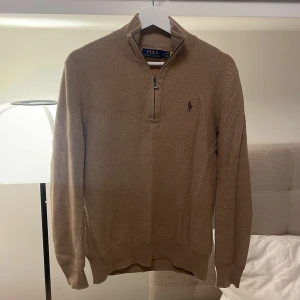Beige half zip tröja från Polo Ralph Lauren - Säljer en beige långärmad tröja från Polo Ralph Lauren med half zip och klassisk broderad logga på bröstet. Tröjan har ribbade muddar och är tillverkad i ett mjukt stickat material som passar perfekt till lager-på-lager-stil.