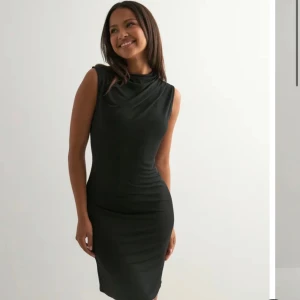 Svart ärmlös kortklänning - Snygg svart klänning med figurnära passform och ärmlös design. Klänningen har en enkel och stilren look med rundad halsringning och slät yta. Perfekt för dig som gillar minimalistisk stil och vill ha något klassiskt i garderoben.