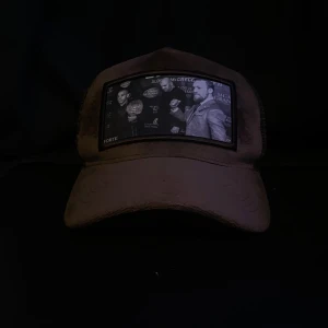 Brun keps från FORTE med UFC-tryck - Säljer en brun keps från FORTE med mesh på sidorna och ett stort svartvitt UFC-inspirerat tryck framtill. Kepsen har böjd skärm och justerbar baksida. Insidan är dekorerad med FORTE-loggor. Perfekt för dig som gillar fighting och streetwear.