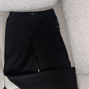 Svarta kostymbyxor från BikBok XS - Svarta kostymbyxor från BikBok i storlek XS. Byxorna har en klassisk rak passform med dragkedja i sidan och är tillverkade i ett mjukt, stretchigt material som sitter snyggt och bekvämt. Perfekta för en clean och stilren look.