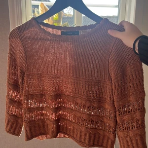 Brun stickad tröja från MNG - Säljer en brun kort stickad tröja från MNG med snyggt virkat mönster och ribbade muddar. Tröjan har lång ärm och är croppad i modellen, perfekt för lager-på-lager. Superskön och trendig till både jeans och kjol.