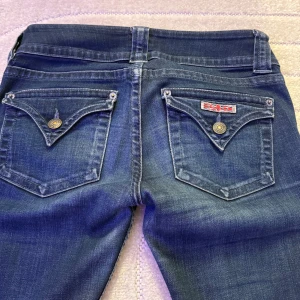 Lågmidjade boot cut jeans  - Snygga mörkblå jeans från Hudson med klassisk bootcut-passform. Jeansen har coola bakfickor med knappar och Union Jack-detalj, samt dubbla knappar framtill. Tillverkade i mjukt denim-material för en bekväm känsla passar , storlek 25 