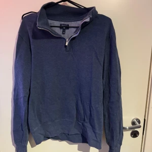 Blå half zip tröja från GANT - Säljer en stilren blå långärmad tröja från GANT med half zip-dragkedja och hög krage. Tröjan har en klassisk passform och är tillverkad i mjukt bomullsmaterial, perfekt för lager-på-lager under kyligare dagar.