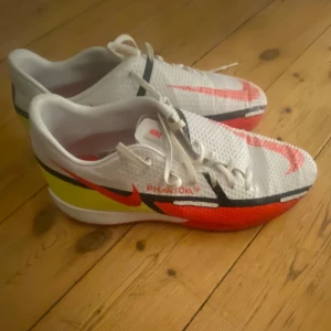 Nike Phantom futsalskor strl 41 - Hej! Säljer ett par Nike Phantom futsalskor i storlek 41 i vitt med röda, svarta och gula detaljer. Knappt använda och enda tendensen till slitage är att färgen skavts bort pyttelite på höger sko fram (se sista bild). Perfekta nu när futsalsäsongen börjar nalkas runt hörnet. 😊