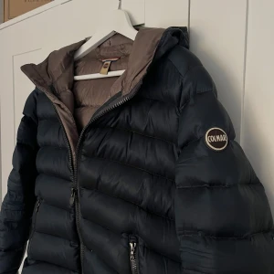 Svart Colmar pufferjacka med huva - Säljer en blå pufferjacka från Colmar med huva. Jackan har en quiltad design och Colmar-logga på ärmen. Perfekt inför vintern, är i väldigt bra skick 