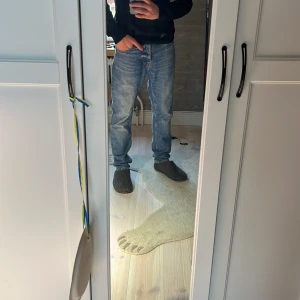 Blå jeans från Nudie Jeans - Säljer ett par klassiska blå jeans från Nudie Jeans med snygg tvätt och raka ben. Jeansen har fem fickor, orangea sömmar och läderpatch bak i midjan. Tillverkade i bomull med en normal passform och midja. Perfekta för en avslappnad stil.