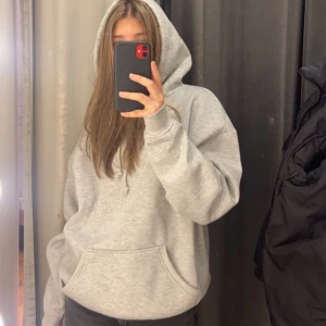 Grå oversized hoodie med huva - Säljer en grå oversized hoodie med huva och snörning. Tröjan har en stor magficka och ribbade muddar vid ärmslut och nederkant. Perfekt för chill dagar och enkel att matcha med jeans eller mjukisbyxor.