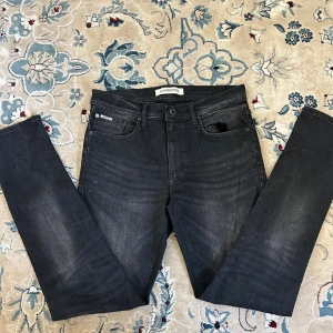 Svarta jeans från Lindbergh - Snygga svarta jeans från Lindbergh med diskret tvättad look. Klassisk femficksmodell med raka ben och normal passform. Jeansen har svarta knappar och detaljer samt Lindbergh-logga på fickan. Perfekta för en stilren och avslappnad outfit.