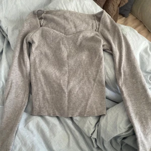 Grå ribbad långärmad topp - Säljer en stilren grå ribbad topp med lång ärm och snygg v-ringad skärning vid bysten. Toppen är figurnära och har en croppad passform som passar perfekt till jeans eller kjol. Materialet är mjukt och stretchigt för en bekväm känsla. Vet ej märke men tror shein 