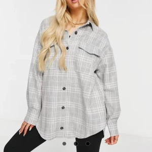 Grå rutig overshirt från ASOS DESIGN - Snygg grå overshirt från ASOS DESIGN i rutigt mönster. Skjortan har svarta knappar, två bröstfickor med lock och en avslappnad, oversized passform. Perfekt att slänga över en t-shirt för en chill look.