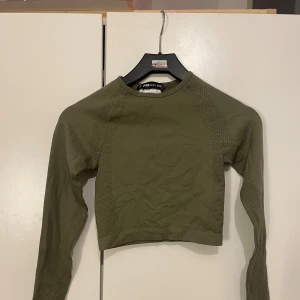 Olivgrön croppad träningströja - Säljer en olivgrön croppad träningströja från Better Bodies. Tröjan har lång ärm, tight passform och ventilerande mesh-detaljer längs sidorna och ärmarna. Perfekt för gymmet eller löprundan.