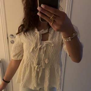 Vit blus med knyt och struktur - Superfin vit blus med puffärmar och tre knyt framtill. Blusen har en vågig, strukturerad yta och är lätt utsvängd nedtill.