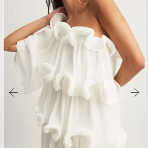 Vit oneshoulder volangklänning - Unik vit kortklänning med asymmetrisk oneshoulder-design och stora volanger över hela klänningen. Luftigt tyg med struktur som ger ett coolt och konstnärligt uttryck. Perfekt för dig som vill sticka ut och älskar statement-plagg med mycket rörelse.