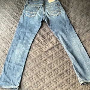 Blå Replay jeans straight fit - Säljer ett par klassiska blå jeans från Replay med raka ben och snygga detaljer på bakfickorna. Jeansen har normal passform och är tillverkade i slitstarkt denimtyg. Perfekta för dig som gillar en tidlös och avslappnad look.