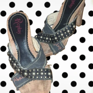 Replay sandaler med nitar och klack - Snygga Replay sandaler-klackar ifrån 90 talet med träfärgad klack och breda svarta remmar i denim och skinn. Remmarna är dekorerade med stora silverfärgade nitar och Replay-logga broderad i rött. Öppen tå och plattformsula ger en cool och edgy vibe.