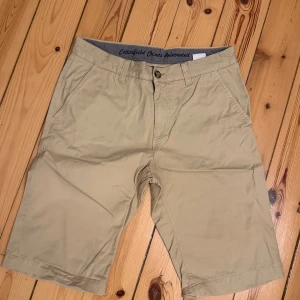 Beiga bomullsshorts från Cottonfield - Snygga beiga shorts från Cottonfield i 100% bomull. Klassisk rak modell med normal passform, bälteshällor, knapp och dragkedja framtill samt fickor både fram och bak. Perfekta för varma dagar och enkel att matcha med det mesta. Storlek 32.