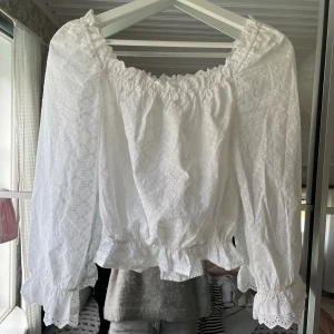 Vit broderad blus  - Vit blus från H&M i storlek 36. Blusen har broderade detaljer, volang vid ärmslut och nederkant samt resår vid halsringning och midja. Långärmad och lätt croppad modell. 