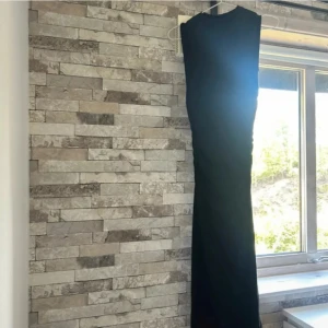 Svart långklänning från Gina Tricot - En stilren svart långklänning från Gina Tricot med ärmlös design och rund halsringning. Klänningen har en figurnära passform och är perfekt för dig som gillar en enkel men snygg look. Materialet känns mjukt och följsamt mot kroppen.